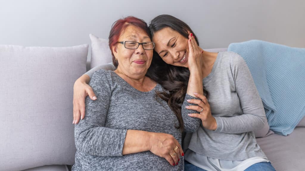 Happy beautiful older Asian mother and adult daughter embracing looking at camera smiling senior