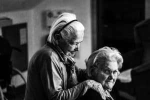 Greyscale Photo Of Woman Standing Behind Woman Sitting On Chair